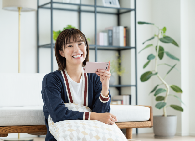 女性がソファーに座って笑顔でスマホを見ている